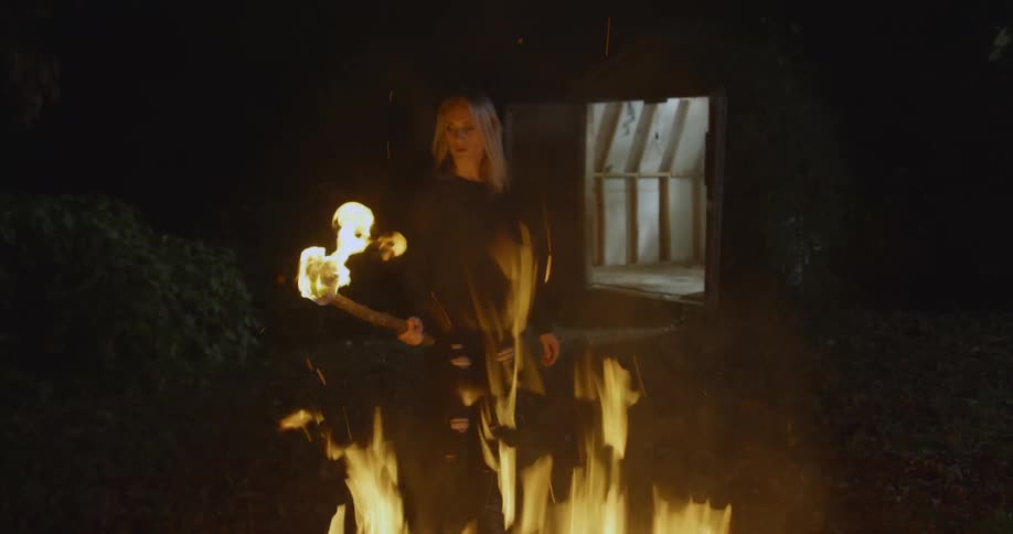 A woman grabs a burning torch from a campfire