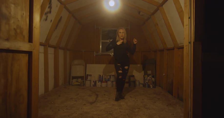 Woman dances in a small room underneath a lightbulb