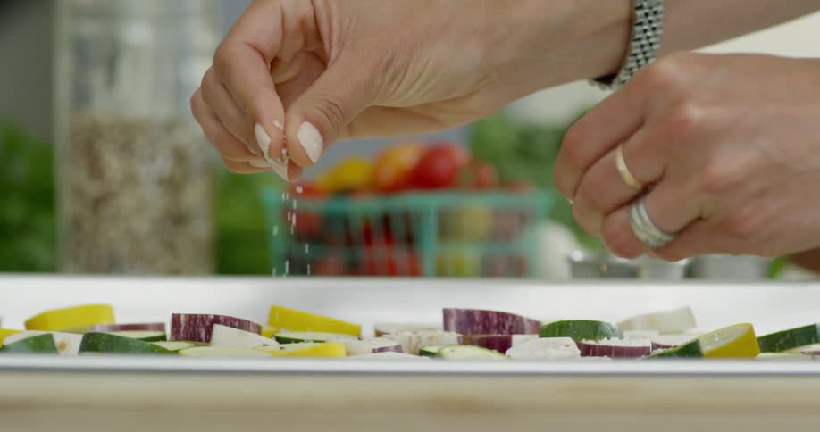 A person is sprinkling salt over the food on the tray