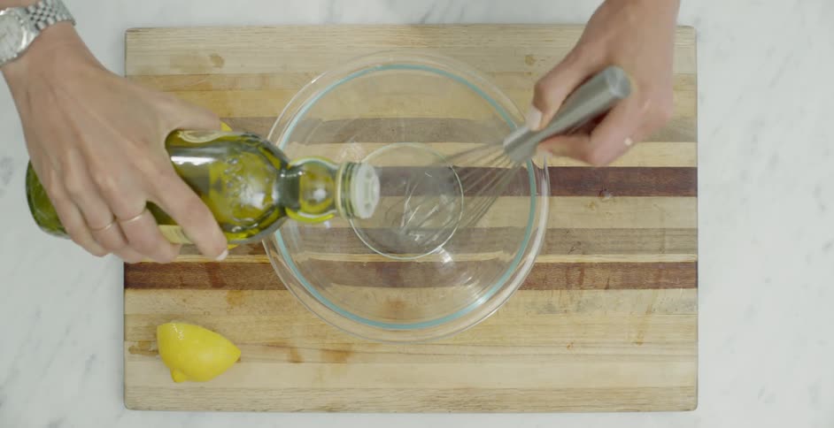 A person is squeezing lemon into a bowl then blending it with oil