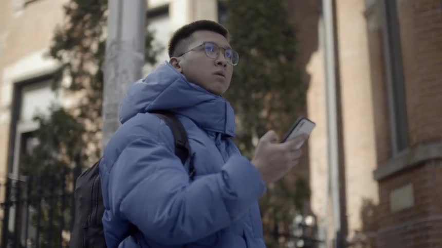A man is checking his cell phone as he walks in a city neighborhood in winter