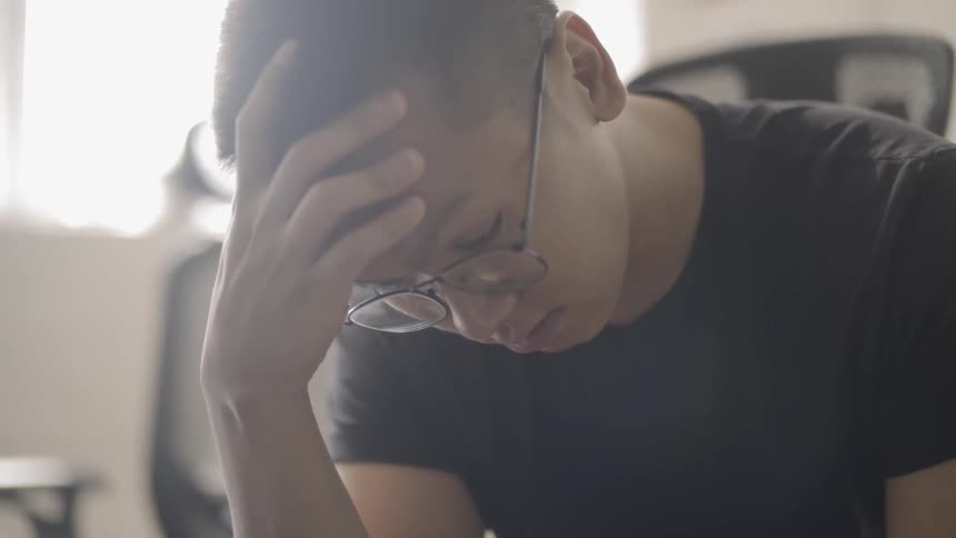 Man wearing glasses rubs his forehead as he looks down