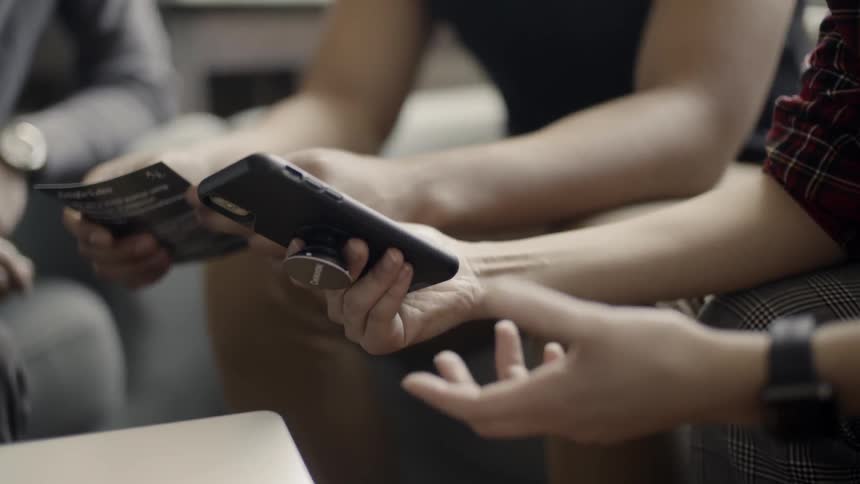 Group of people are sitting looking at cell phone and talking