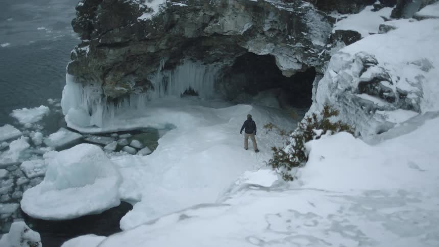Person walks on hilly snow towards the mouth of a cave