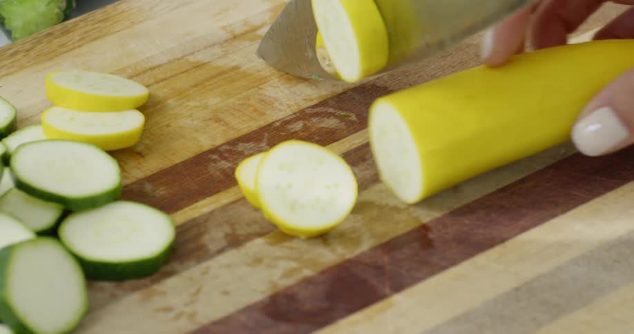 A woman is cutting squash on a cutting board in daylight