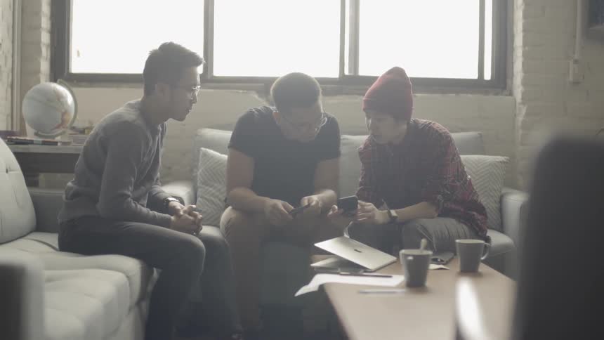Three  men sit on couches and look at one man's phone