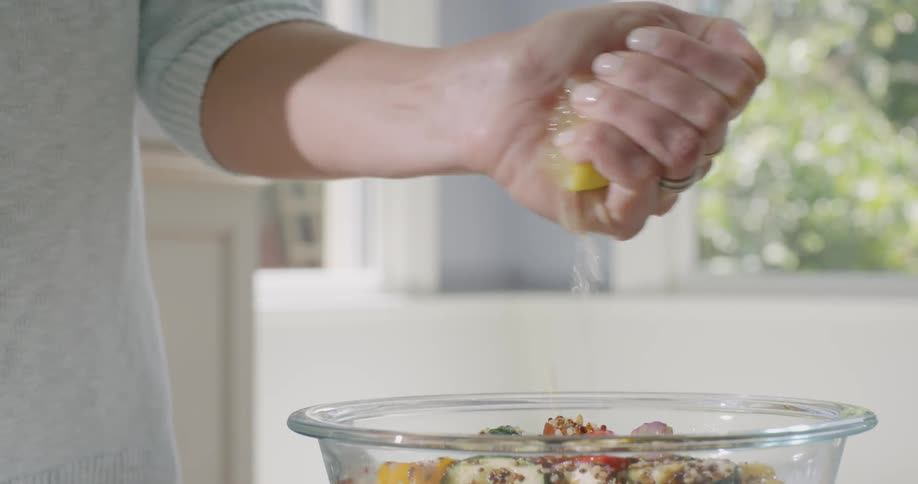 A woman squeezes lemon juice onto food in a bowl