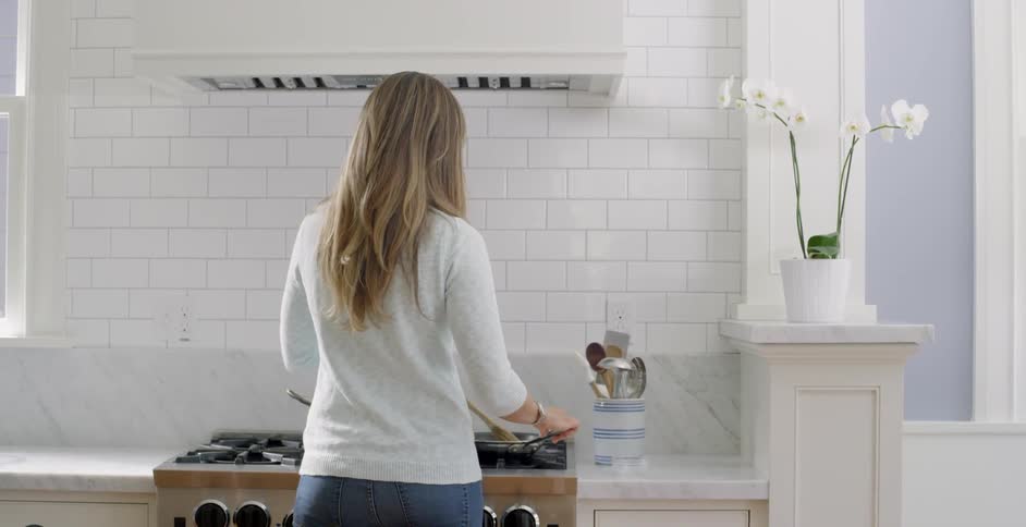 Woman standing at stove in kitchen is stirring food in pan