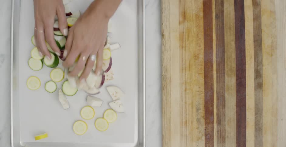 Woman is gathering sliced vegetables onto baking sheet