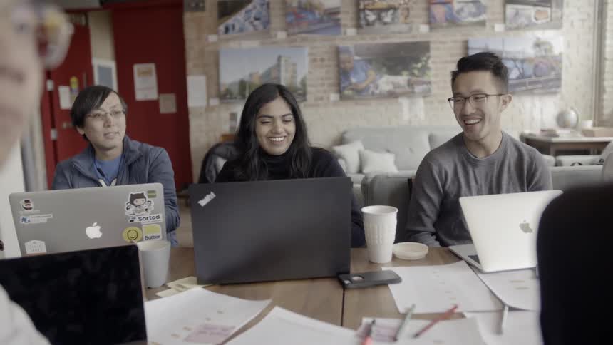 Men and women sit around a table each with a laptop in front of them