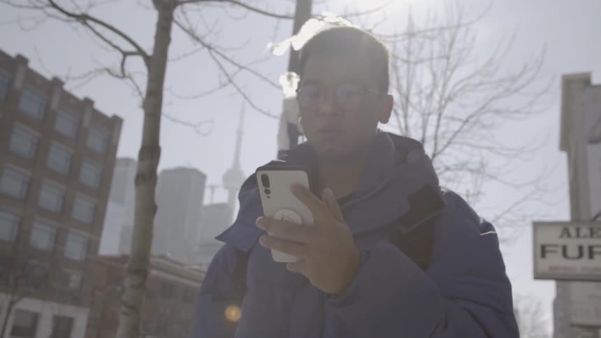 A man looks at his phone as he walks on a city sidewalk