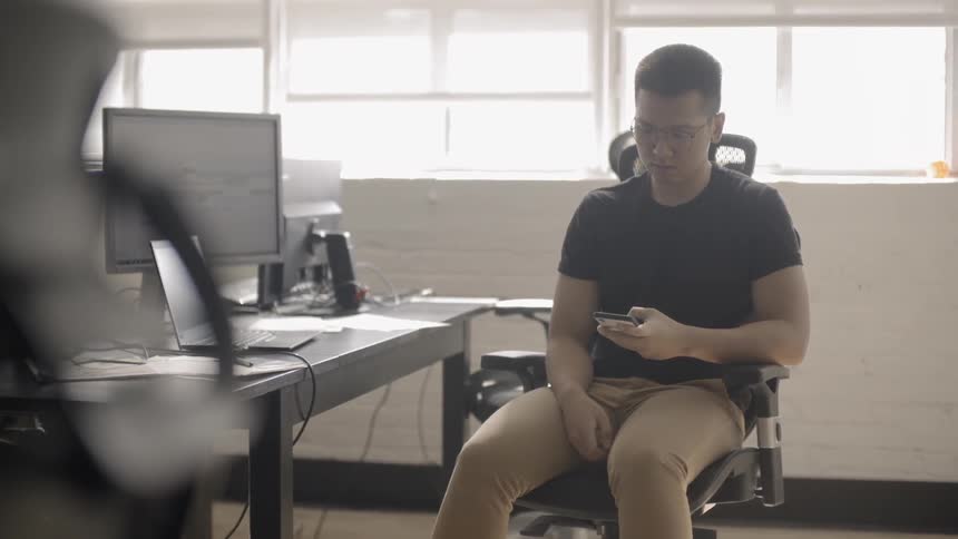 Man talks on a phone next to a table with a laptop and monitor on it