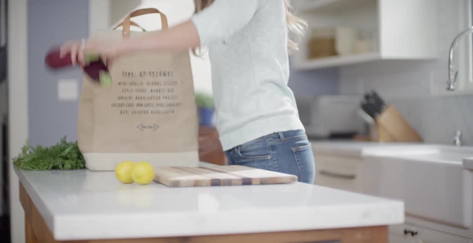 A woman is standing inside her kitchen in daylight unpacking groceries