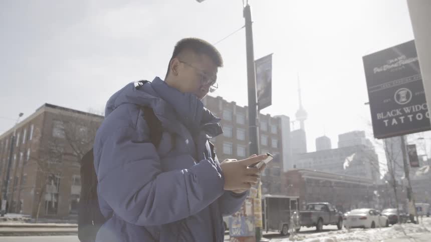 A man is checking his cell phone as he walks in a city in winter
