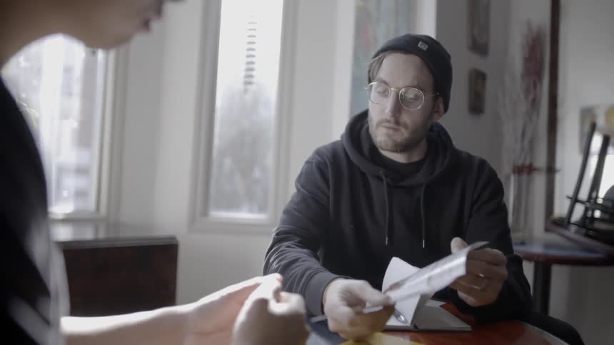 Two men talk at a table and one man hands the other man a piece of paper