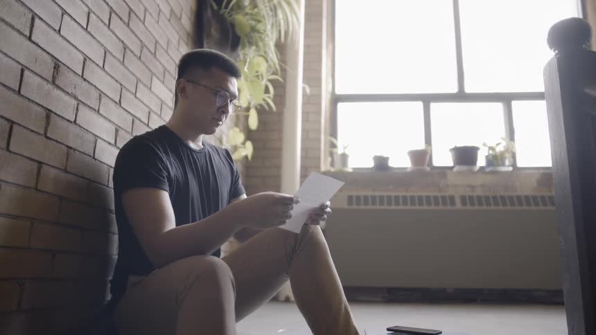 Man sits on the floor as he reads a letter