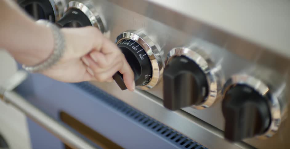 A woman turns a knob on a stove