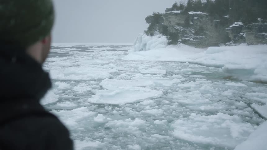 A man watches as ice on the surface of the water floats with the waves