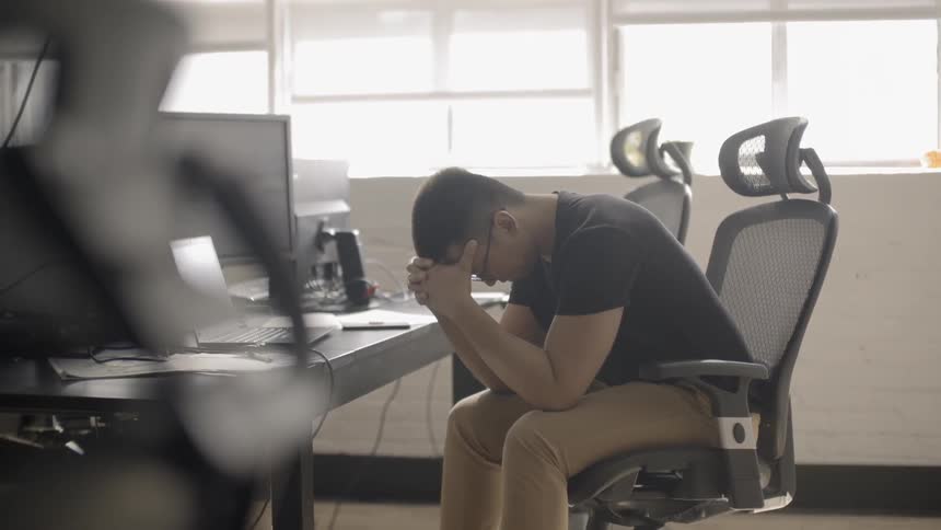 A man sits at an office chair and puts his head in his hands
