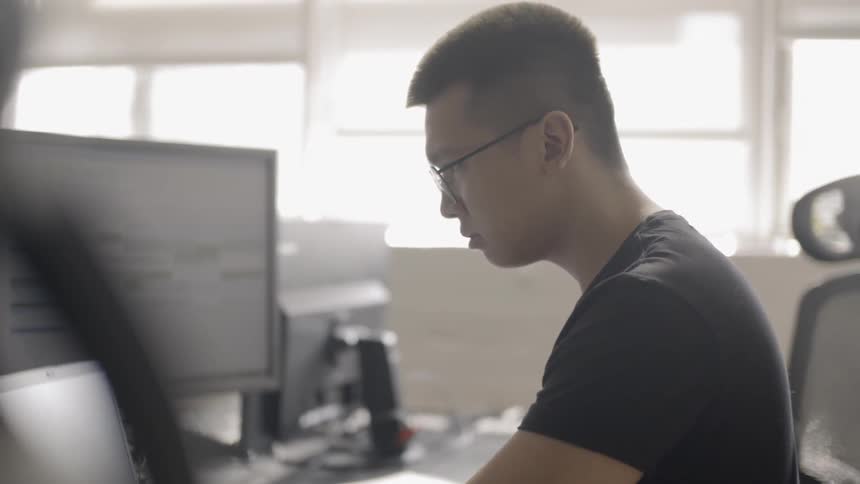 A man is using a laptop as he sits at a desk in daylight