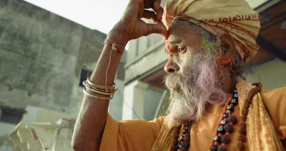 Man wearing a headdress with his thumb pressed to his forehead