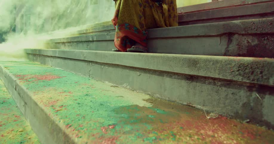A person in traditional indian dress sits on steps that are covered in colored powder