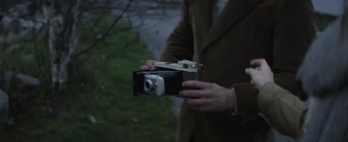 A woman hands an antique camera to a man