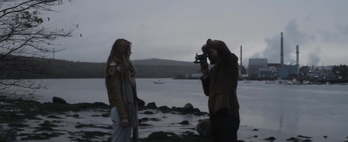 A man photographs a woman standing on the shore