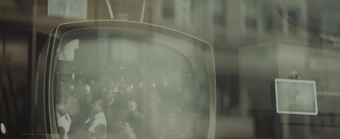 An old tv seen through a shop window displays a crowd of men