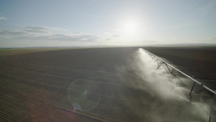 Flying parallel to a farm field irrigation system spraying seedlings on a sunny day