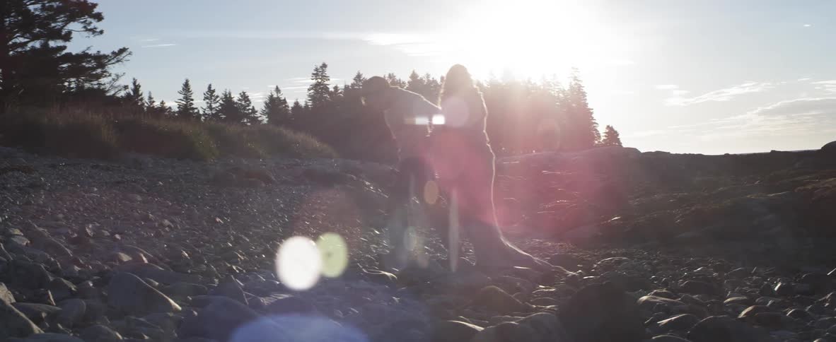 Man and woman walking a rocky shore at sunset