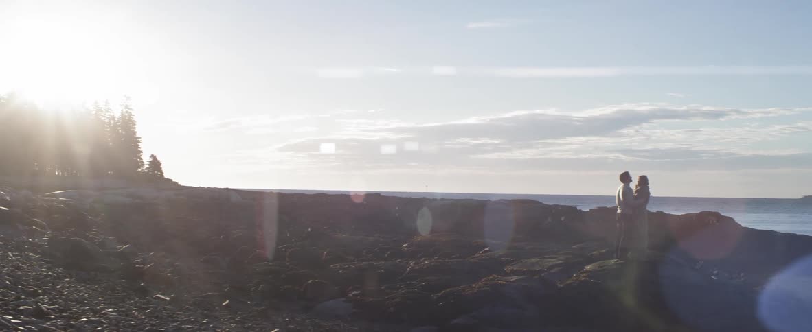 Couple embrace on the rocks as the sun rises