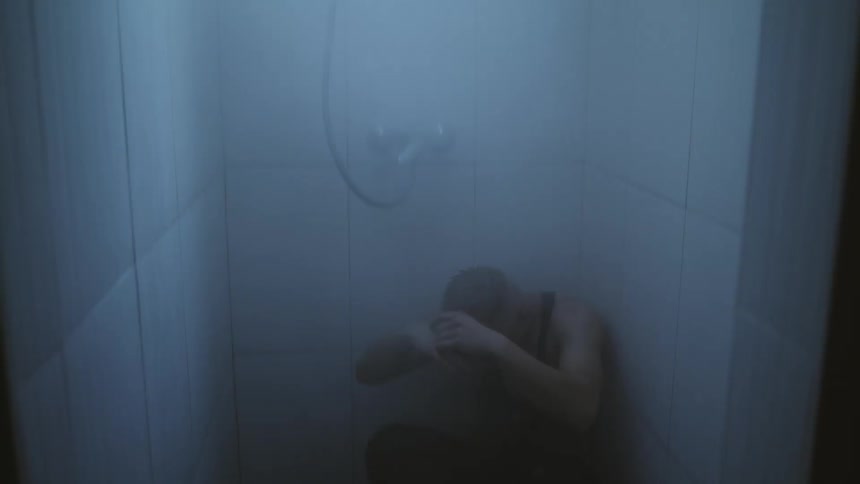 Man sits in the corner of a shower and crosses his arms while lowering his head
