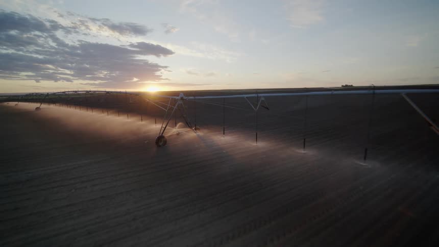 Low pullback reveal of farmland irrigation as the sun sets behind a plowed field