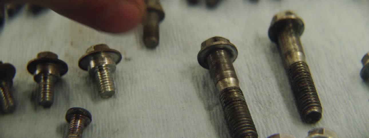 A man is laying out bolts in an arrangement on a surface