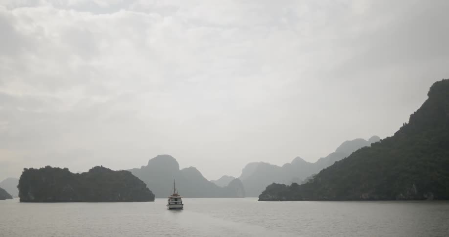Boat cruises on the open water near a hill and large rock formations