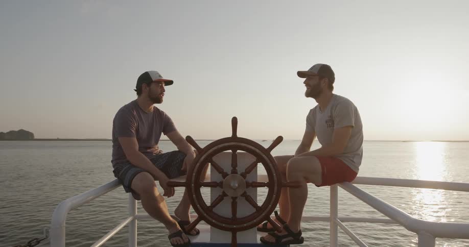 Two men sit on the railing of a boat