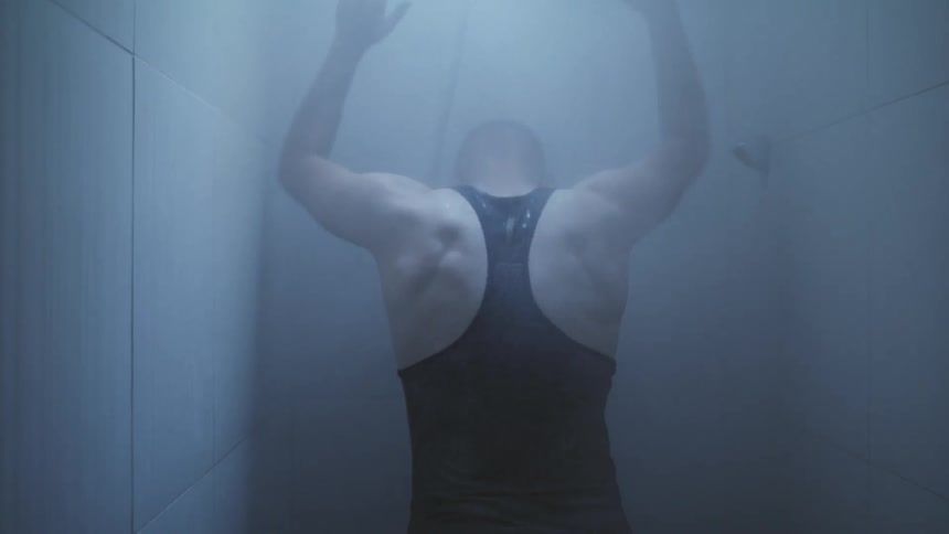 A male athlete is walking into a running shower and slapping his hands on the walls