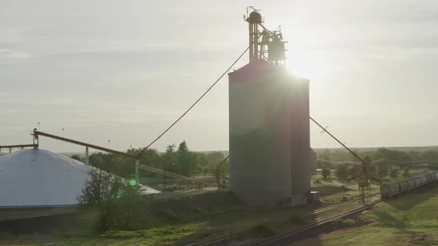 Reveal of a grain storage facility as the sun sets behind two tall silos