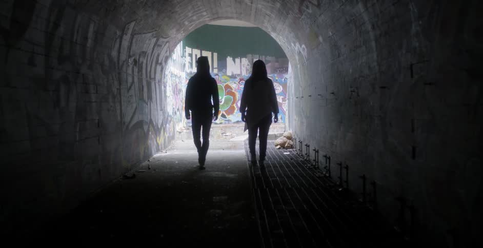 Two women walk through a tunnel with graffiti