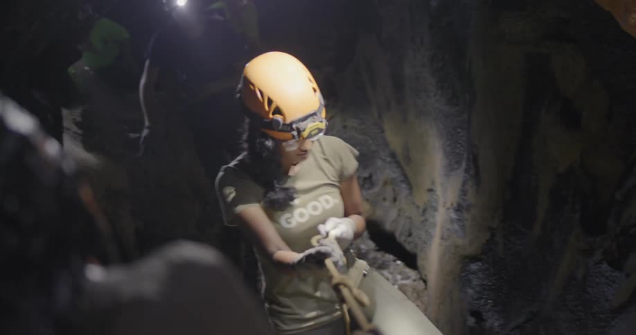 Woman wearing a helmet pulls herself up a rope as she climbs through a cave