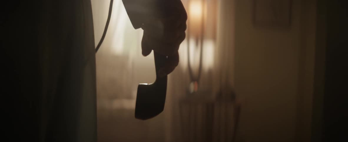 A person walking in a house and holding a telephone earpiece