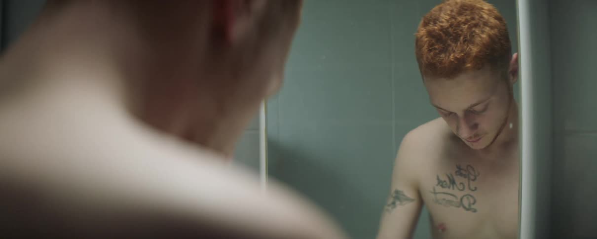 Shirtless man looks at himself in mirror before looking down