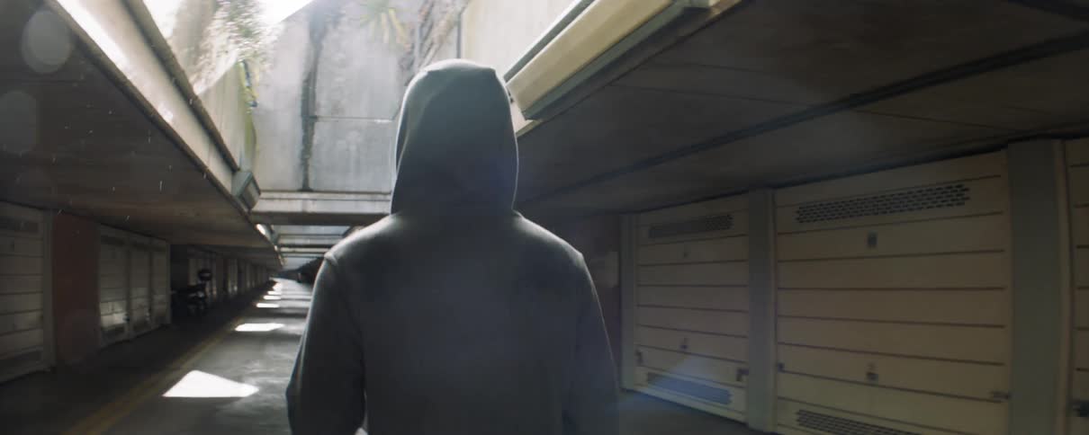 A man wearing a hoodie walks past garage bay doors under a building