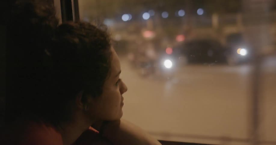 A woman rests her head on her arm as she looks out the window while riding the bus in the city at night