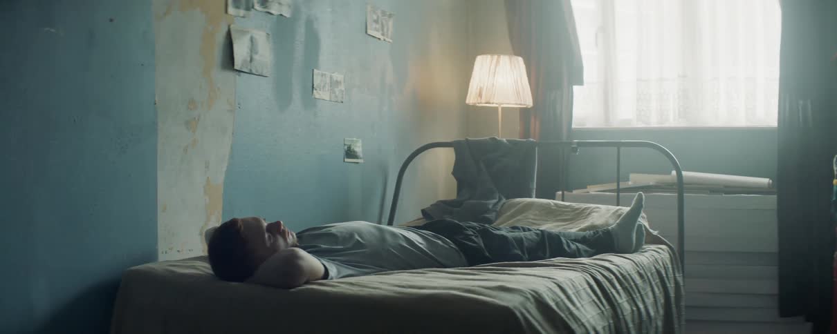 A man is lying on his bed in daylight