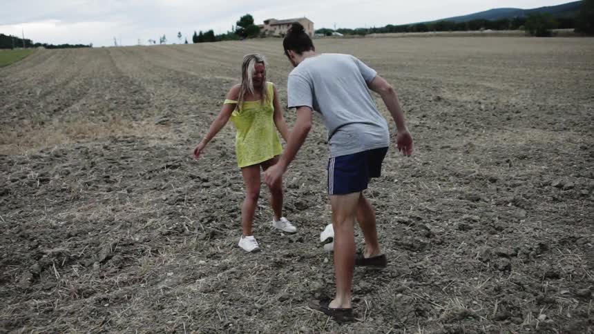 Man and woman are playing with soccer ball in dry field