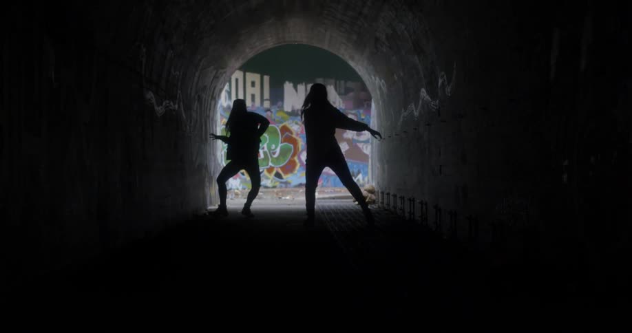 Two women dance in a dark tunnel