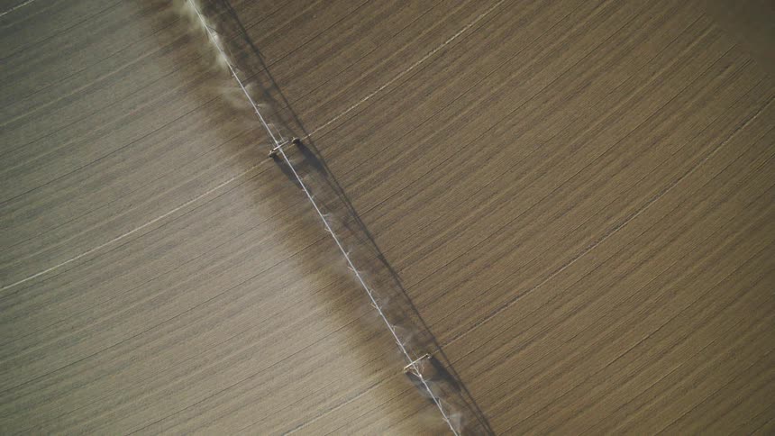 Birds eye view descent of a center pivot irrigation system watering a plowed farm field