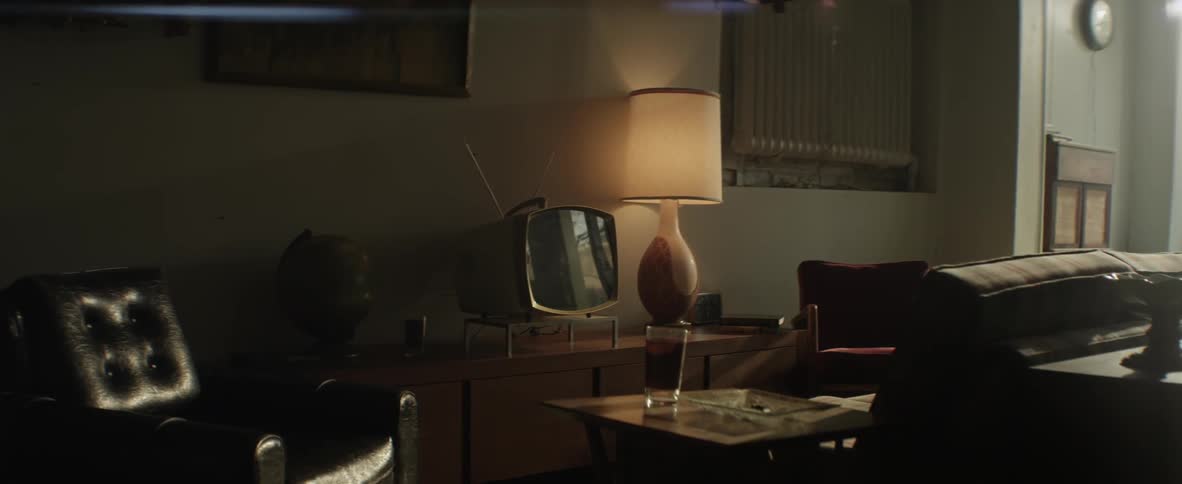 A front room scene that includes a lamp, television, chairs and a tv tray with a drink resting on top